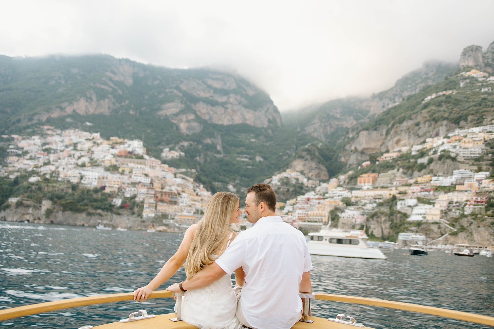 A couple on the bow of a boat, looking back towards Positano
